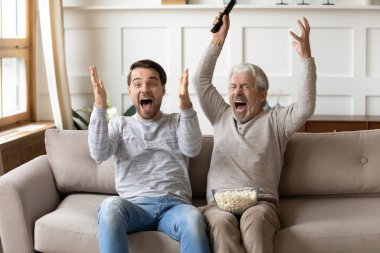 Overjoyed young man watching football match with middle aged father.
