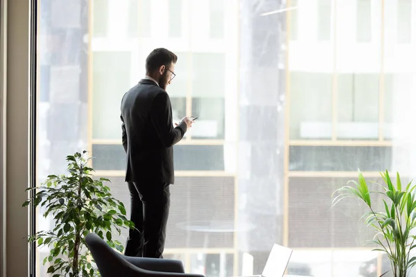 Middle eastern ethnicity businessman standing near panoramic window with smartphone — 图库照片