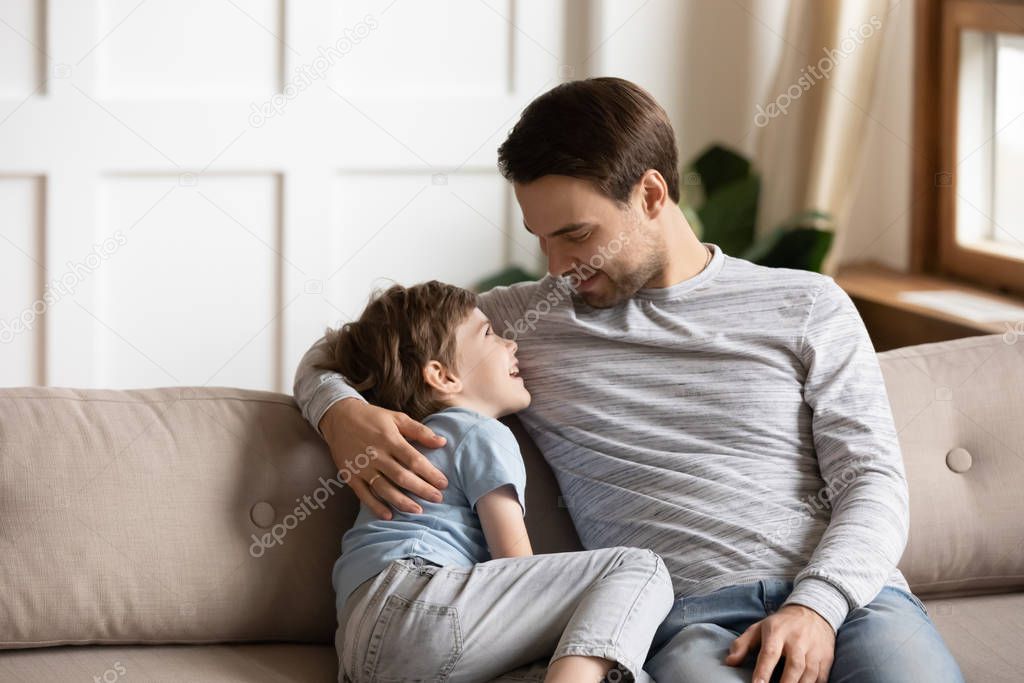 Happy young father embracing little kid son, communicating at home.