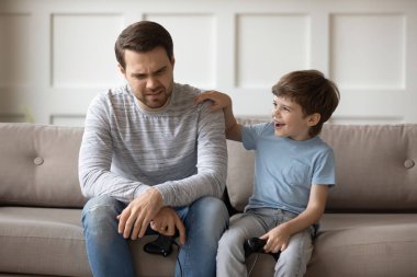 Happy small child supporting upset father after losing video game.