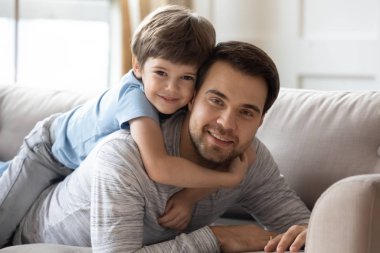 Carefree boy cuddling smiling dad, looking at camera.