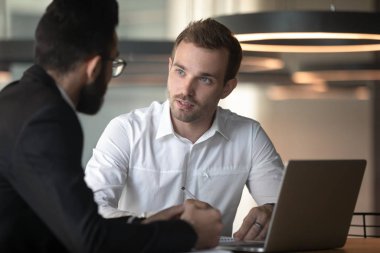 European and arabian male colleagues talking seated at office desk