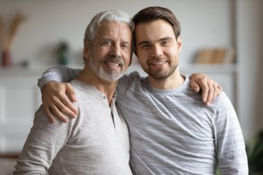 Elderly mature dad cuddling shoulders of grownup son.
