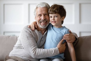 Happy middle aged grandfather embracing little schoolboy at home.