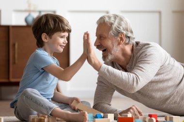 Funny little boy giving high five to joyful older grandfather.