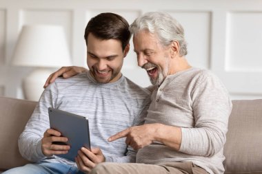 Smiling young man showing funny photo on tablet to father.