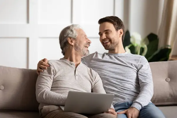 Glücklicher älterer Mann mit Computer genießt lustige Zeit mit Sohn. — Stockfoto
