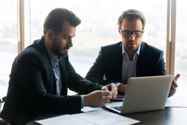 Serious businessman coaching partner looking at laptop screen.