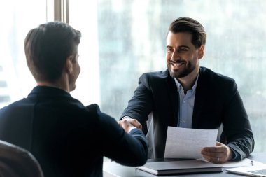 Smiling bearded businessman in suit shaking hands with job seeker.