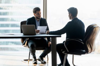 Serious businessman in suit holding cv listening new job candidate.