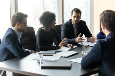 Serious businessman telling diverse employees about project sit at table.