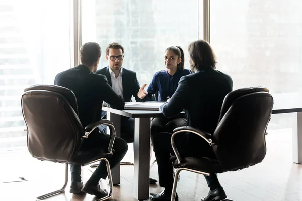 Confident businessman with colleague having heated discussion with partners sitting. — Stockfoto