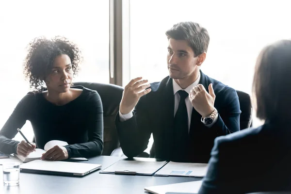 Un hombre de negocios seguro contando a diversos empleados sobre el proyecto se sienta a la mesa . — Foto de Stock