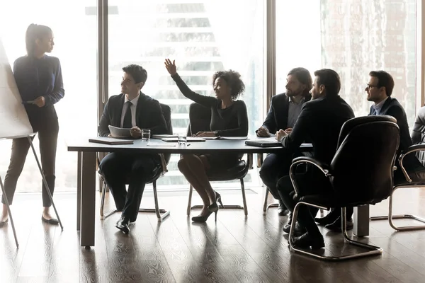 Smiling black businesswoman raising hand asking female lead in boardroom.