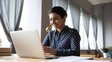 Happy young Indian female busy working on laptop