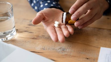 Unhealthy young woman drinking pills at workplace