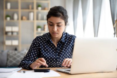 Focused ethnic woman paying bills online on laptop