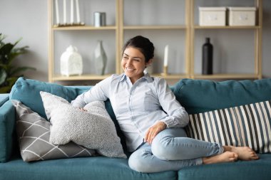 Happy millennial ethnic girl relaxing on sofa at home