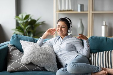 Overjoyed ethnic girl in headphones listen to music