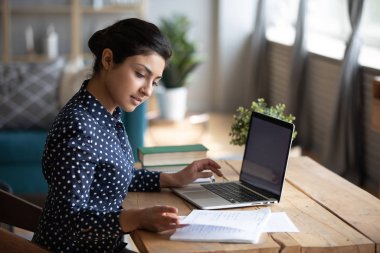 Millennial Indian girl study at laptop making notes