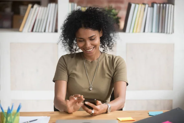 Mujer de negocios afroamericana sonriente que usa aplicaciones de dispositivos móviles en el trabajo —  Fotos de Stock