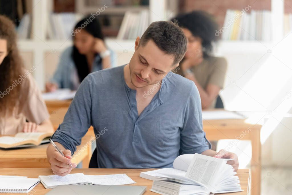 Attractive student studying with textbook in classroom, writing notice