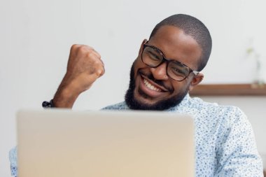 Smiling African American businessman celebrating success, using laptop