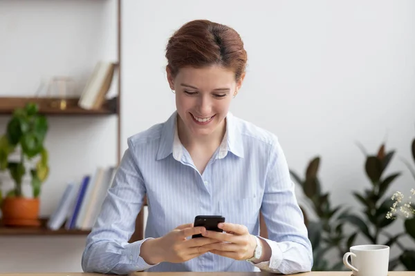 Mujer de negocios sonriente usando teléfono móvil en el lugar de trabajo durante el descanso —  Fotos de Stock