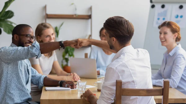 Diverse employees fist bumping, celebrating good work results