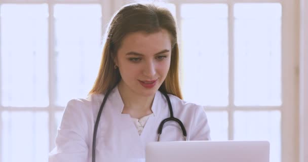 Улыбающаяся женщина-врач носит медицинскую форму с помощью компьютера — стоковое видео