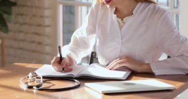 Young woman doctor writing notes in notebook sit at desk