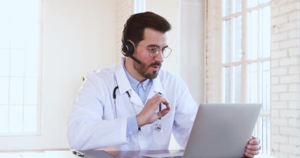 Professionnel mâle médecin porter casque faisant conférence téléphonique médicale sur ordinateur portable — Video