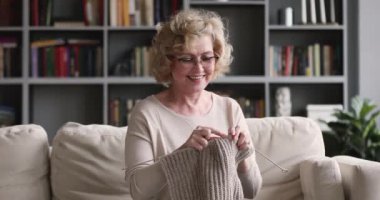 Happy mature older woman enjoying knitting needles looking at camera