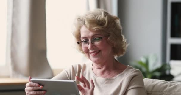 Sorridente signora anziana indossare occhiali ottici utilizzando tablet a casa — Video Stock