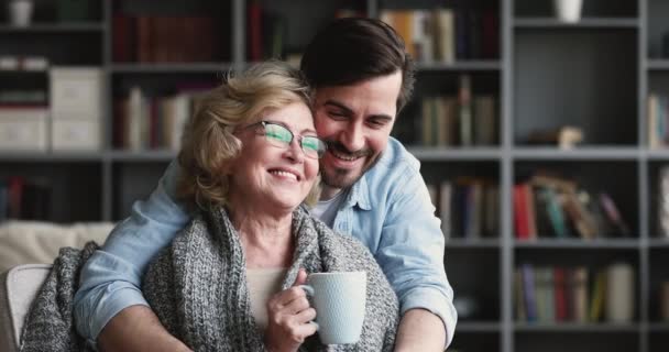 Happy loving adult son embracing old mother drinking tea — Wideo stockowe
