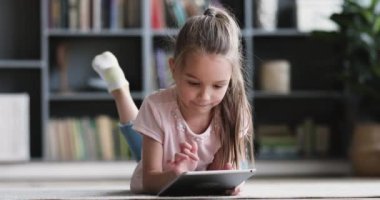 Curious cute preschool girl using tablet lying on carpet alone