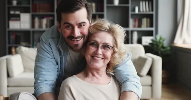 Smiling 30s son looking at camera hugging older mom indoors — Stockvideo