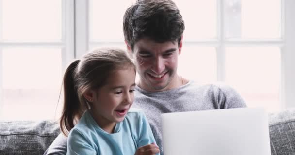 Sonriendo joven papá enseñando a niño pequeño hija riendo usando el ordenador portátil — Vídeo de stock