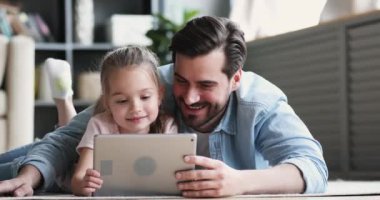 Dad and small daughter using digital tablet lying on floor