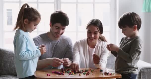 Happy parents and kids playing stringing multicolored beads necklace — Stock videók