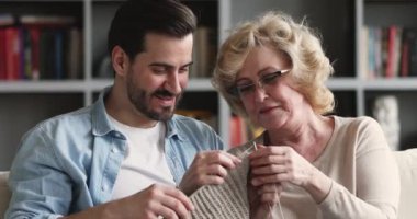 Happy older mother teaching knitting helping young adult son