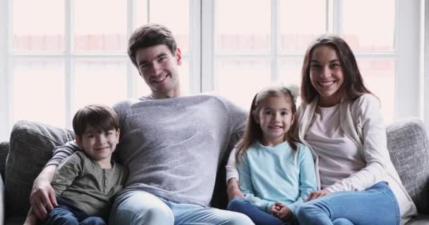 Los padres alegres y los niños miran la cámara cosquillas en el sofá — Vídeos de Stock