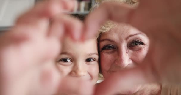 Affectionate grandmother and granddaughter making heart gesture looking at camera — Stock Video