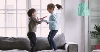 Happy kids boy and girl having fun jumping on sofa