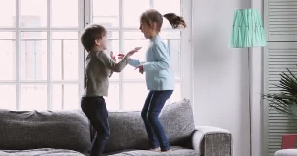 Happy kids boy and girl having fun jumping on sofa — Stockvideo