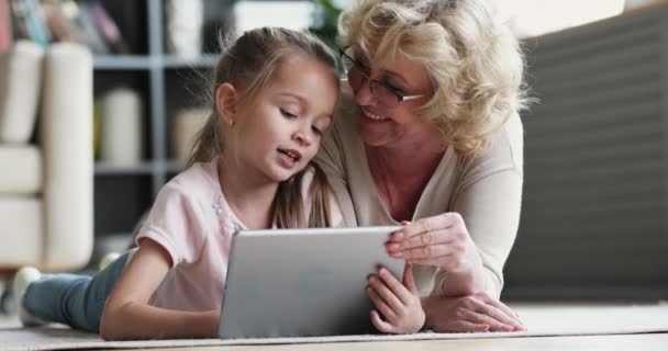 Old grandma teaching preschool granddaughter learning reading ebook on tablet — Stock Video