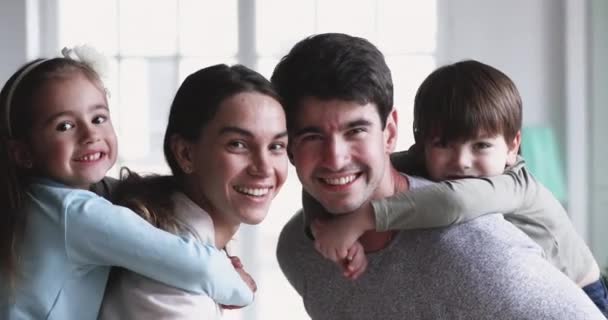 Feliz padres piggyback lindo niños mirando la cámara en casa — Vídeo de stock