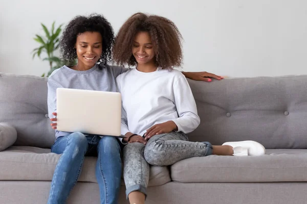 Feliz madre africana e hija adolescente utilizando el ordenador portátil en el sofá — Foto de Stock