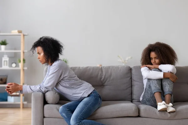 Annoyed african single mother and upset daughter sit on sofa