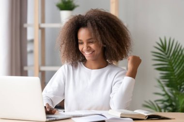 Heyecanlı neşeli Afrikalı genç kız öğrenci dizüstü bilgisayara bakıyor.